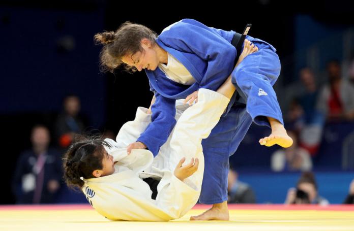 Two female Para judo athletes in a bout. Sandrine Martinet, who is wearing a blue judogi, is throwing her opponent